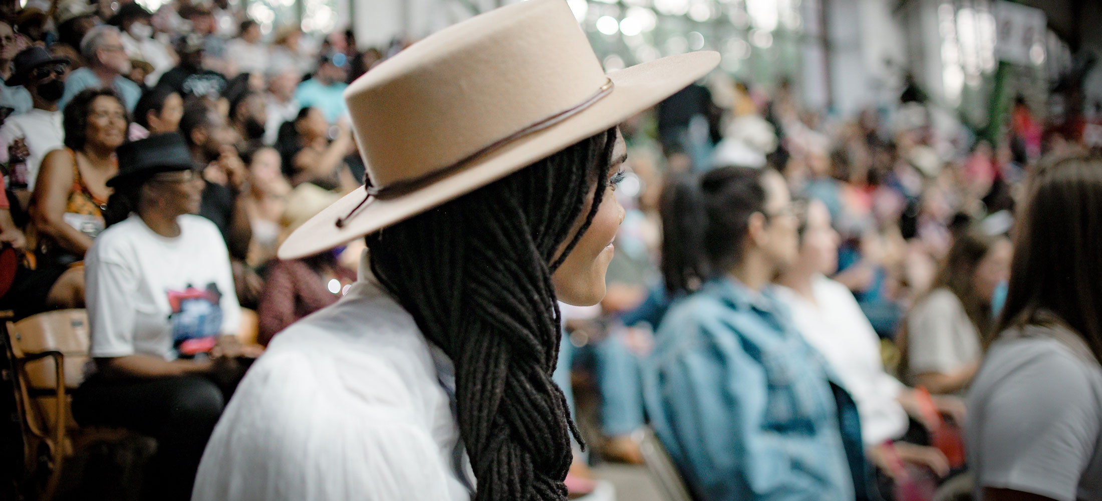 A woman sitting in a crowd at a rodeo looking away from the camera wearing a tan felt hat